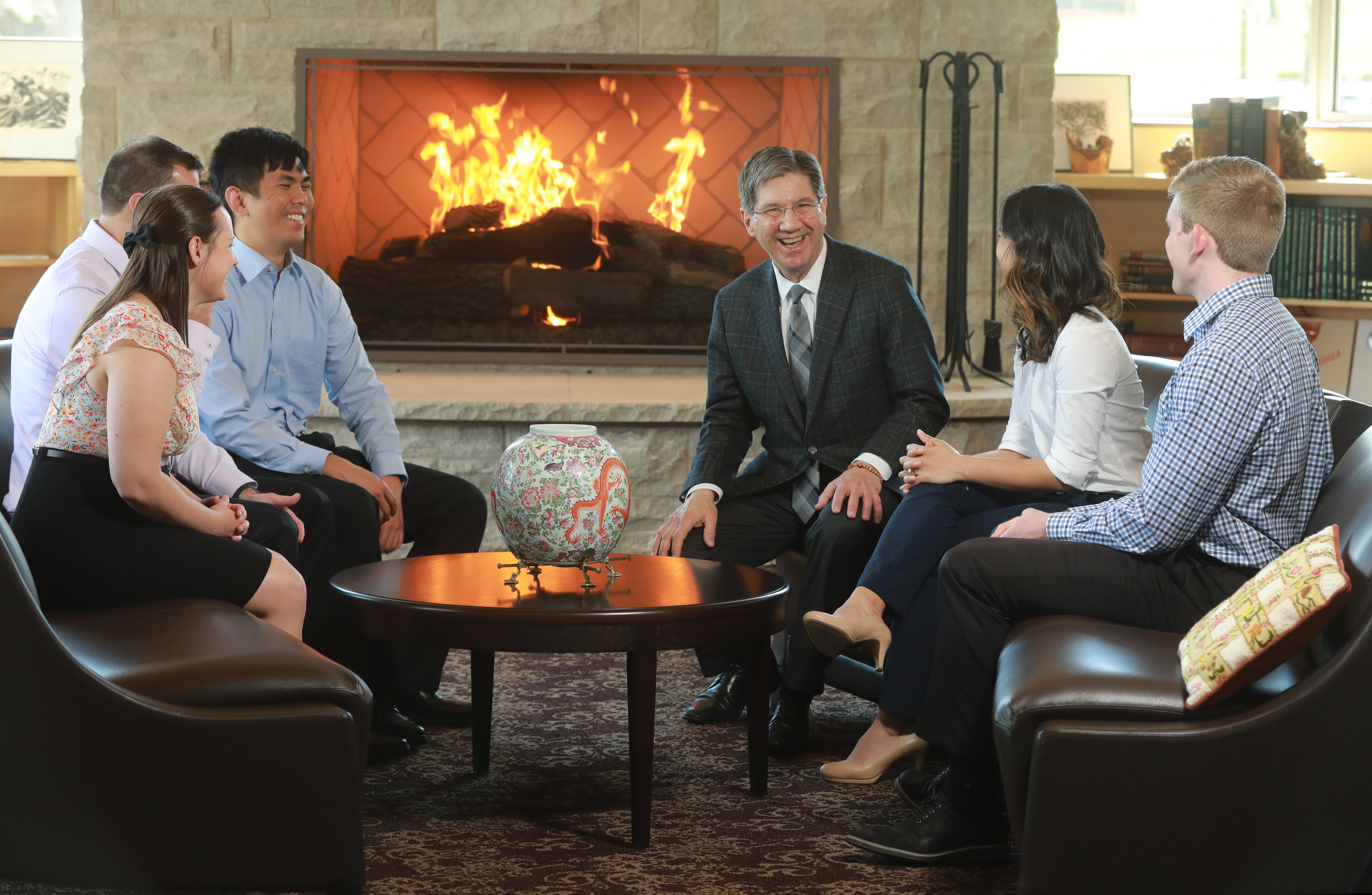 Dr. Nemitz sitting with students in front of fire in presidents parlor. All students face the president, he seems to be laughing.