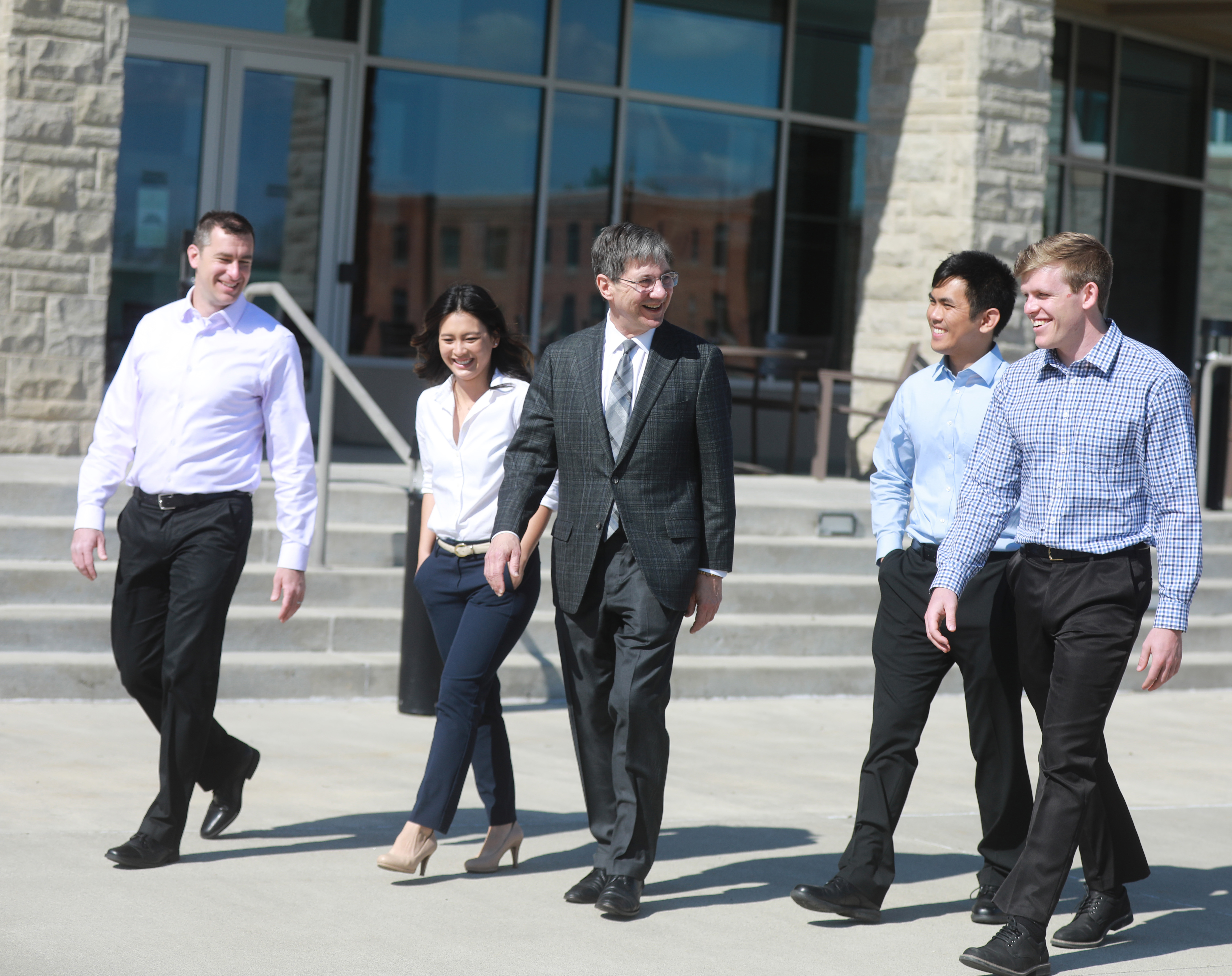 Dr. Nemitz walking on sunny campus day with 4 visitors to campus, two on each side. All appear happy and laughing/smiling.