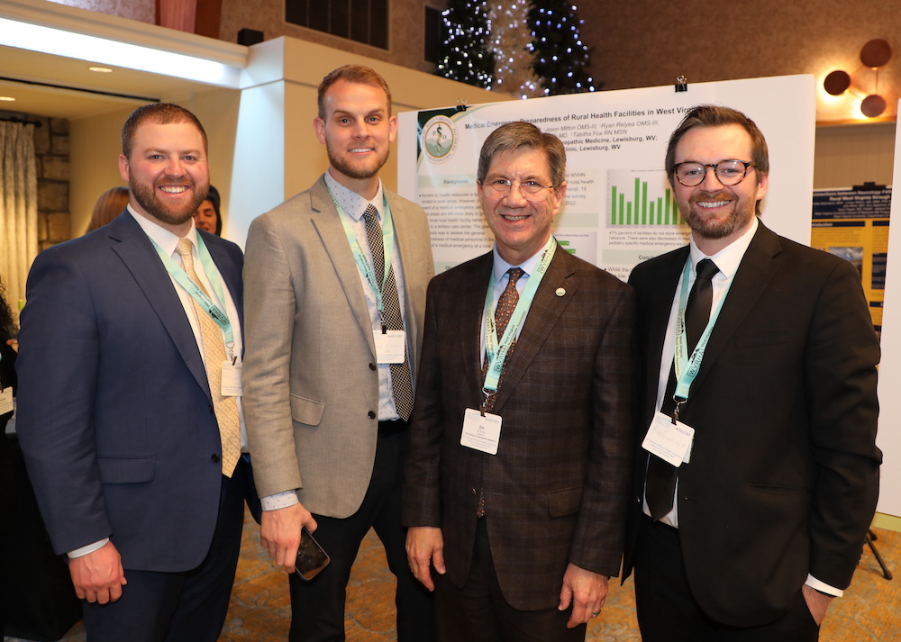 Students Porter Green, Jason Mitton, and Ryan Relyea stand with WVSOM President James W. Nemitz at their poster display. 