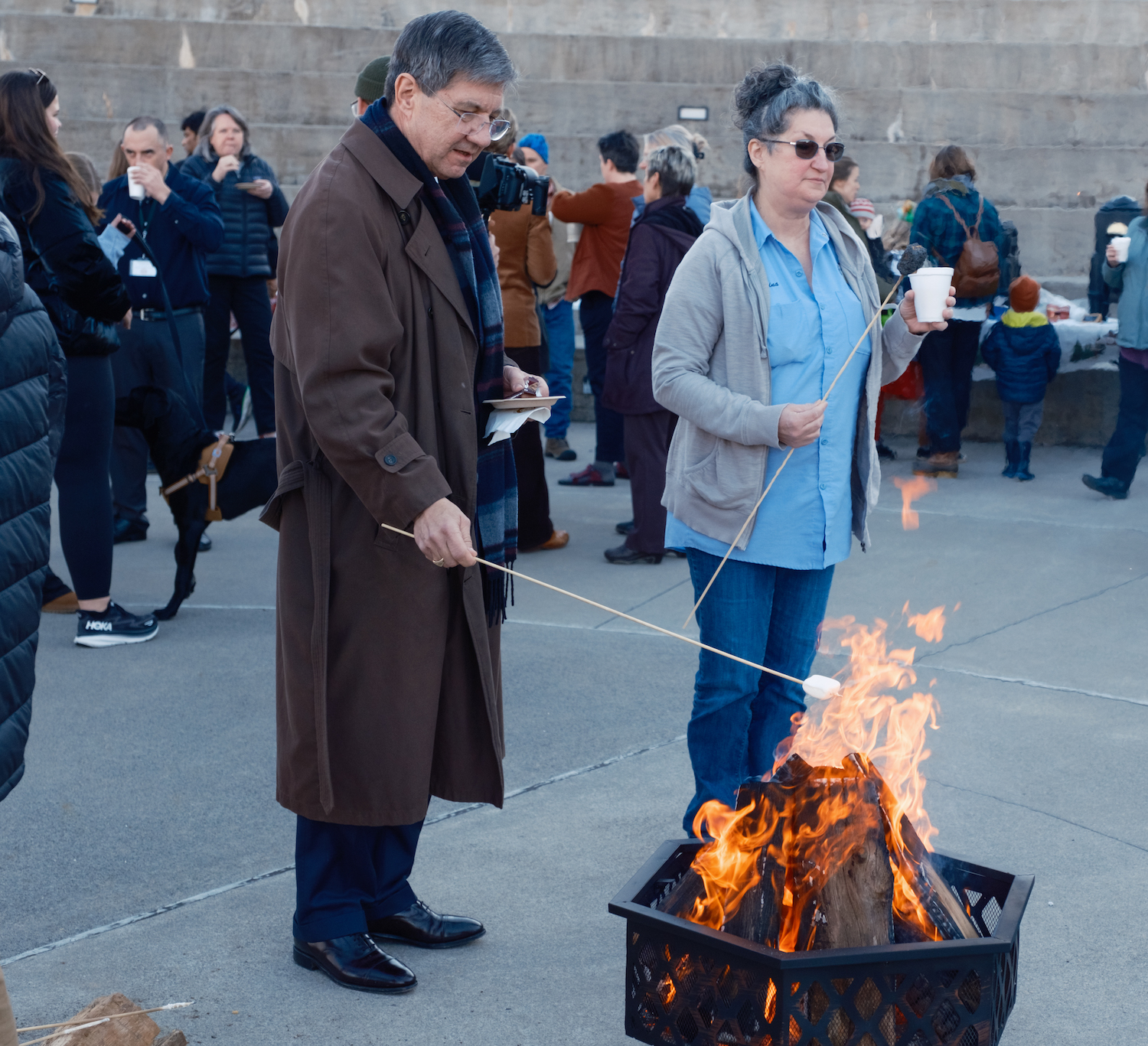 Dr. James Nemitz stands roasting a marshmallow next to campus service worker Gina Griffin who has finished her marshmellow.