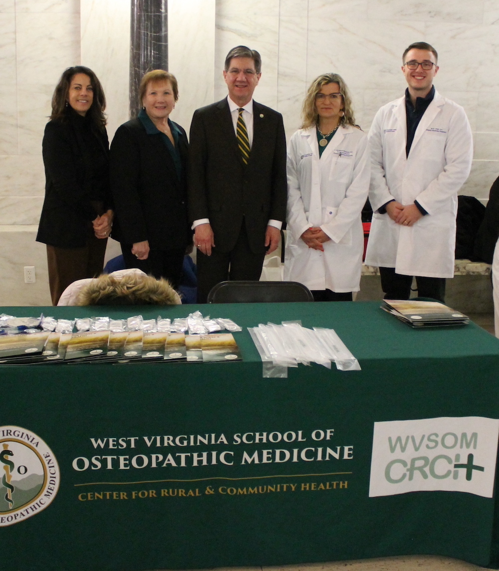 Five people line up shoulder to shoulder in front a table with a WVSOM banner.