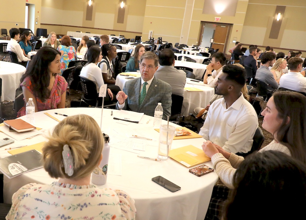Man talks to a group at a table in a large room filled with people