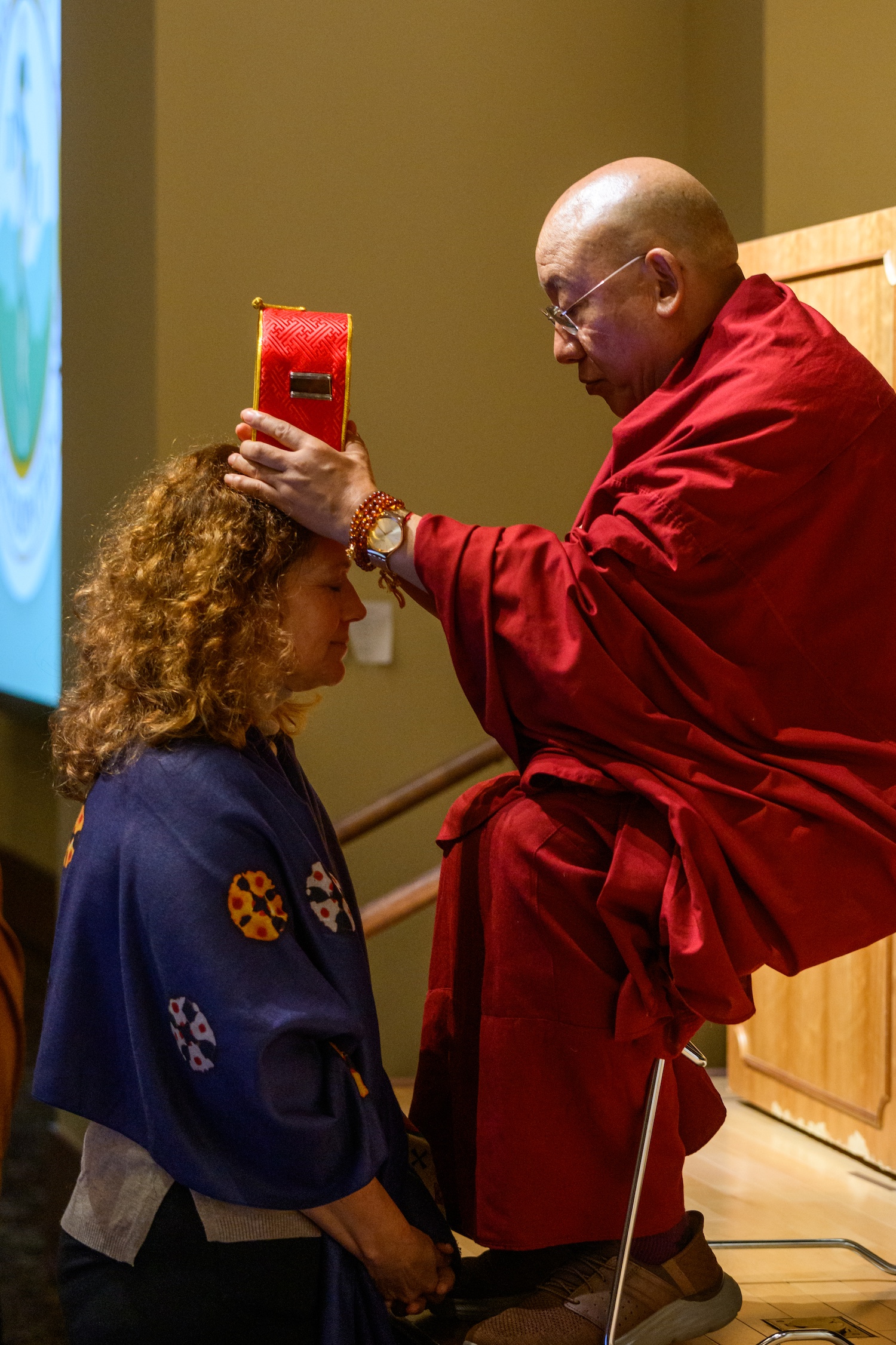 Seated man touches head of woman who is kneeling in prayer