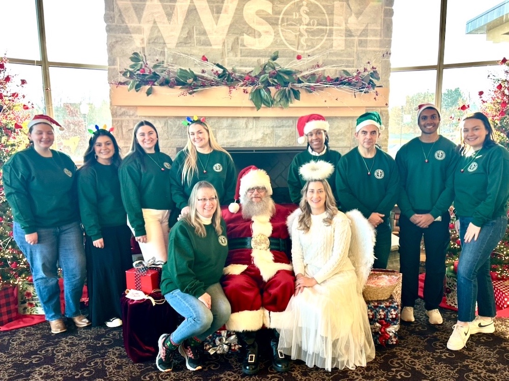 Large group of people in matching shirts sitting around Santa and an angel