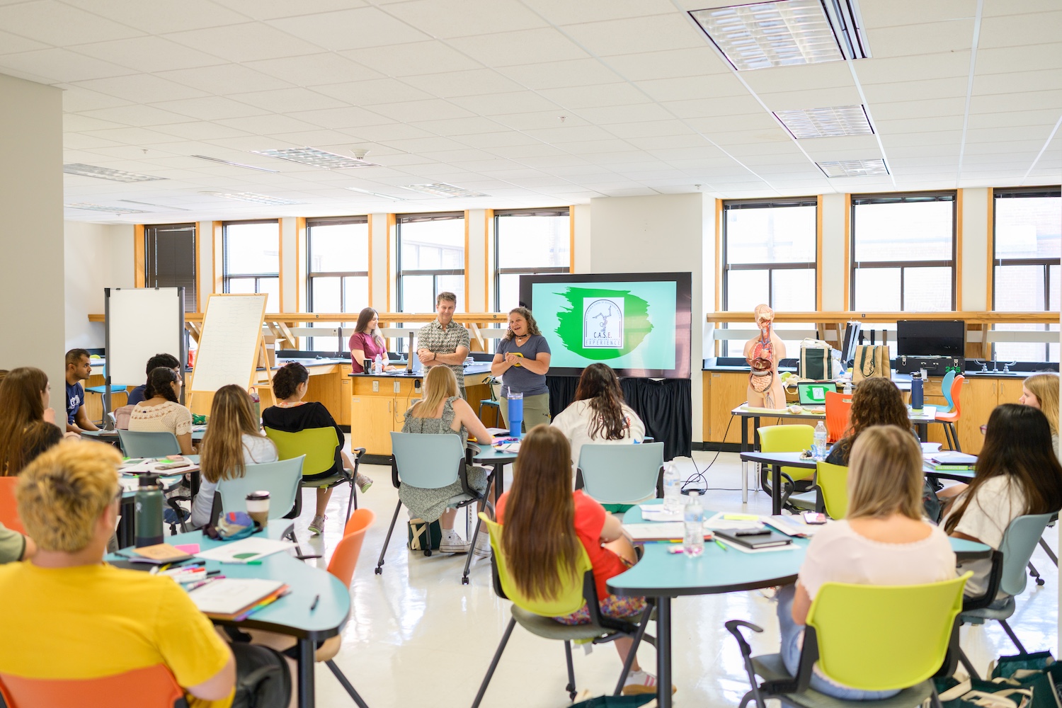 People sit in a classroom and list to one person talking at the front of the room.