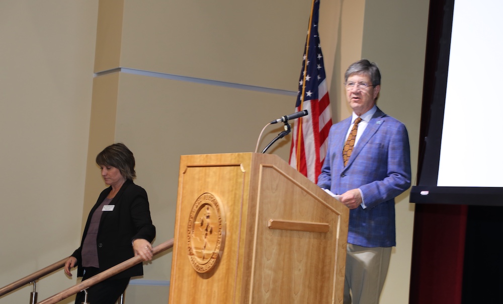 Man stands a podium as woman leaves the stage. 