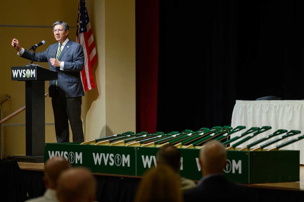 Man stands at a podium near a line of shovels