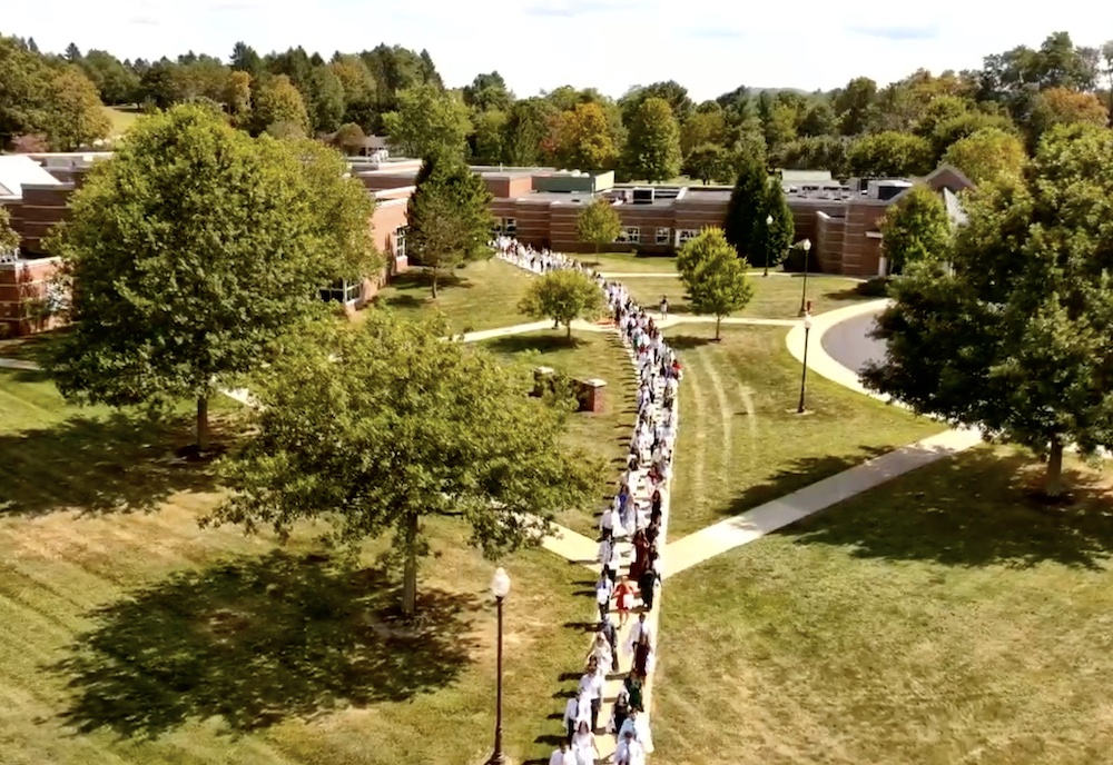 long line of students marching across a grassy lawn