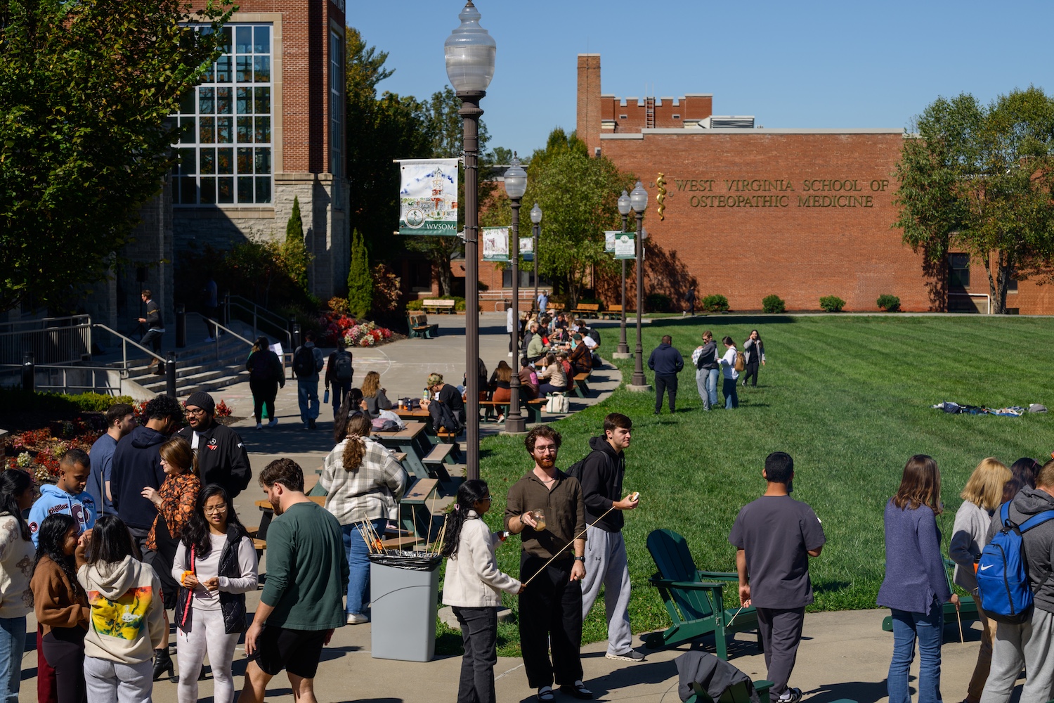 A large group of people stand along a building and grassy lawn on a sunny day.
