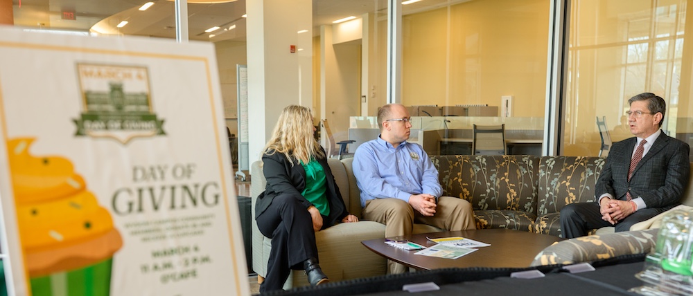 woman and two men sit and talk. 