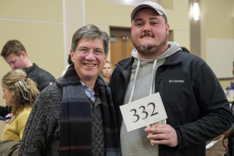 two men stand together holding a small sign with an auction number printed on it.