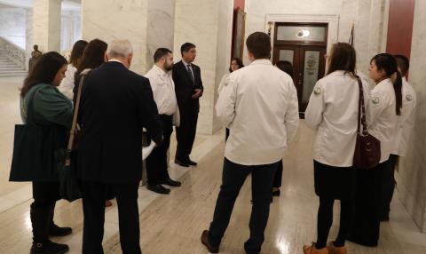 A goup of people in suits and students stand in a circle and talk.