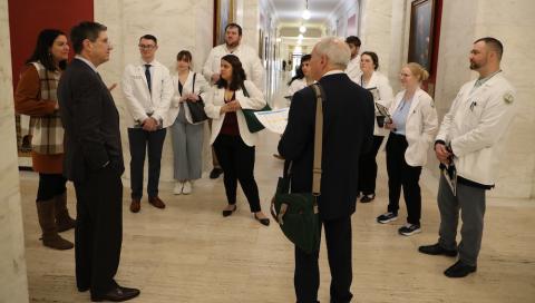 A woman and two men talk with a group of students in a long hallway