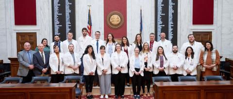 24 people in two rows pose for a photo in the capitol. 