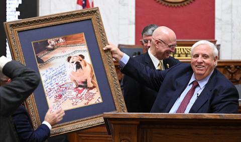 Man, seated, displays large portrait of his dog. 