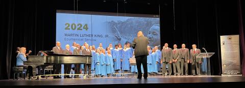 Stage is filled a line of people performing as a choir. 