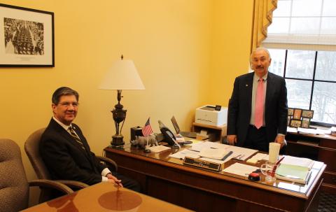 Two men, one seated and one  standing, talk. 