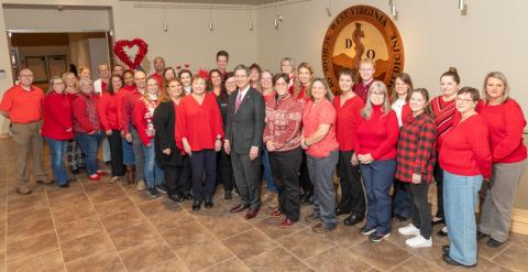 Large group of people, lined up in front of a sign, all wearing some piece of red clothing.