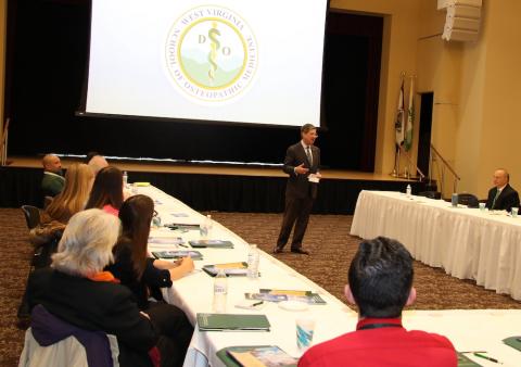 Man stands in middle of a room talking to seated people