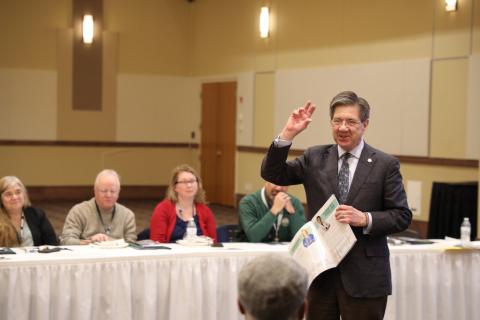 Man standing in a room talking to seated people