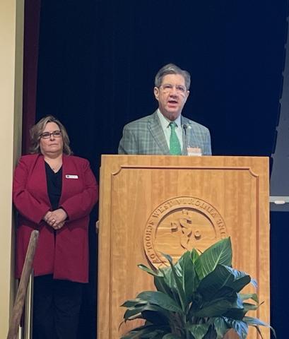 Man stands at a podium. A woman stands to this left. 