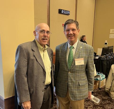 Two men in suit jackets stand shoulder to shoulder.