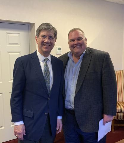 two men in suits stand shoulder to shoulder.