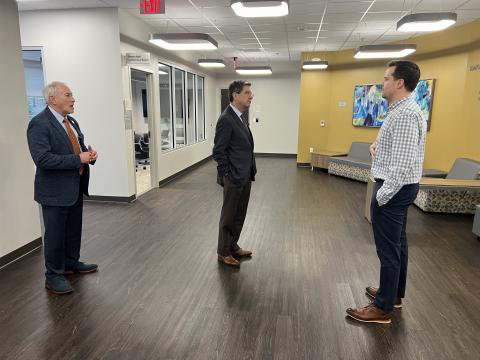 three men in suits stand in a hallway