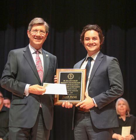 Two men stand, holding a plaque.