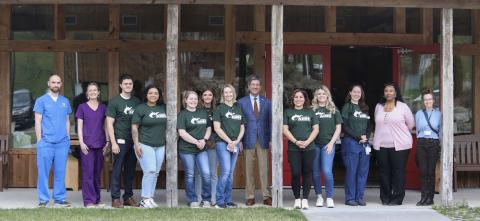 Horizonal line of 13 people facing the camera while standing on a porch. 