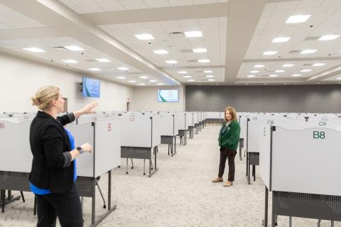 Two women talk in large room. 