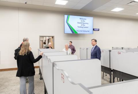 Group of people stand in a room of desks. 