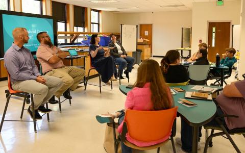 four people seated in the front of a room talk to a room of people