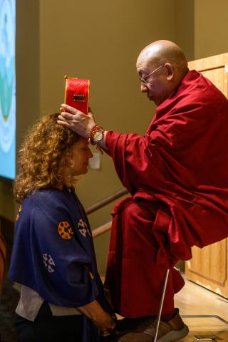 Seated man touches head of woman who is kneeling in prayer