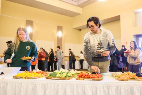 Woman and a man stand at a table of veggies with other people walking in the background