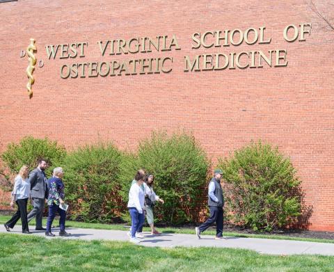 People walk in front of brick wall with WVSOM sign