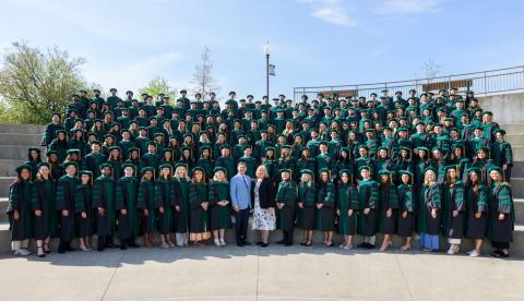 Large group of people in gaps and gowns on steps. 