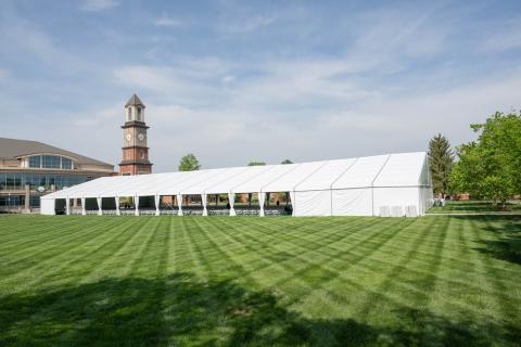 large tent on grassy field with clock tower in the rear