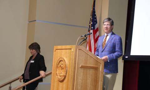 Man stands a podium as woman leaves the stage. 