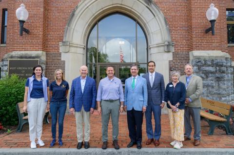 Eight people stand in a line in front of a building. 