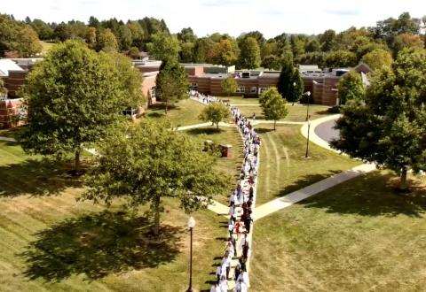 long line of students marching across a grassy lawn