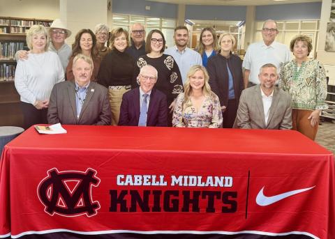 Four people sit at a table and 12 stand behind them. 