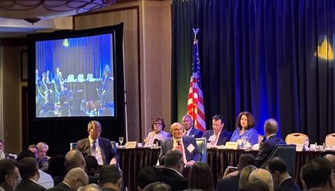 Three men on a stage in a room full of people