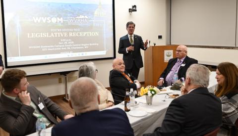 Man stands in front of table and talks to several guests