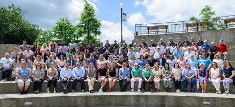dozens of people sit on concrete stadium seating for a photo. 