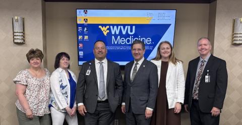 Six people line up in front of a WVU sign