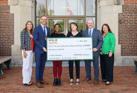 Six people hold up a large check signifying a fund-raising success.