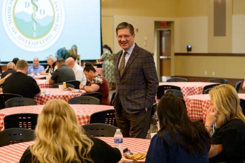 a man in a suit walks around people seated at tables. 