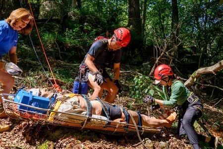 three students work with a Manikin on a stretcher in the wilderness