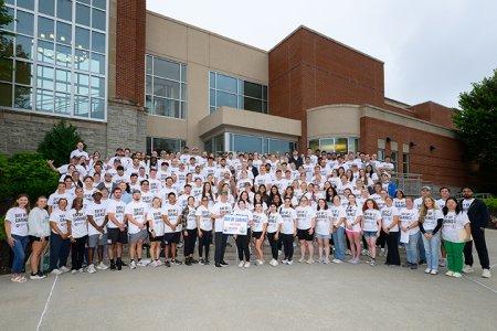 more than 200 students in white T-shirts stand on steps for a photo.